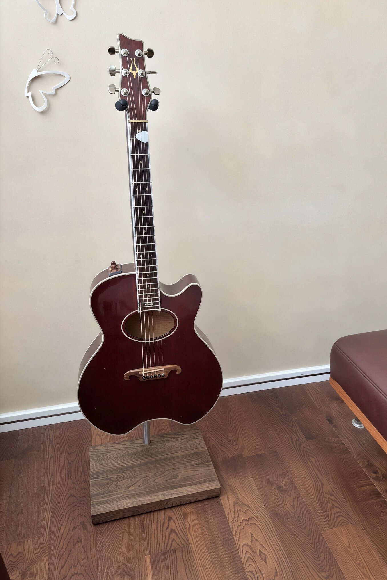 Burgundy acoustic guitar on a premium handmade stand with a solid wood base in a minimalist interior.