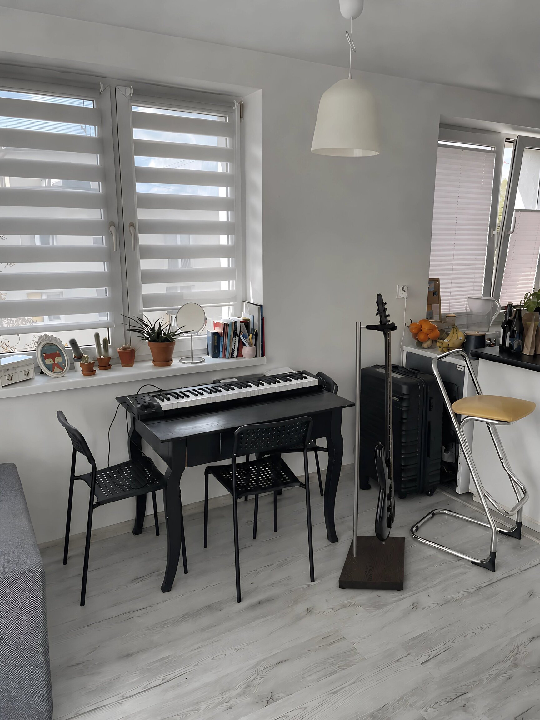 Black electric guitar on a luxury wooden stand in a bright apartment beside a digital piano and open kitchen.