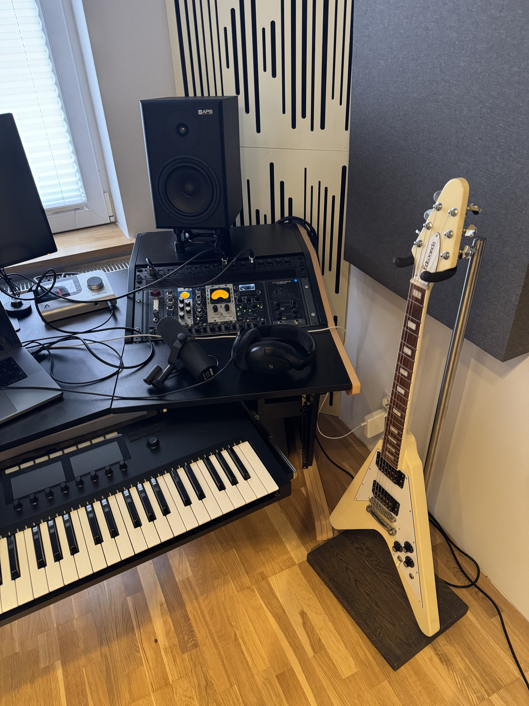 Handmade electric guitar stand with a dark solid wood base beside a music production desk in a home recording studio.
